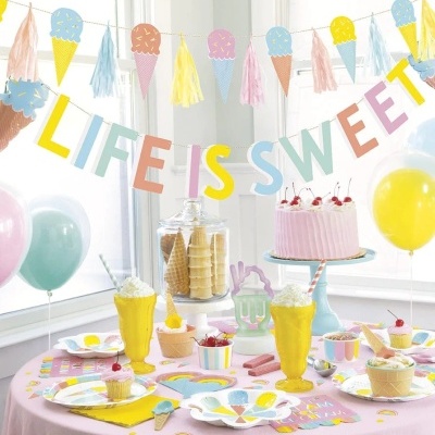 Decoração de festa com tema de gelados em tons pastel e mesa com bolo e sobremesas.