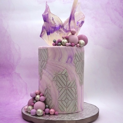 Bolo decorado cilíndrico em tons roxos com padrão geométrico e esferas coloridas