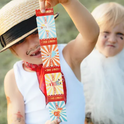 Criança vestida com chapéu de palha mostra bilhete colorido com texto ADMIT ONE
