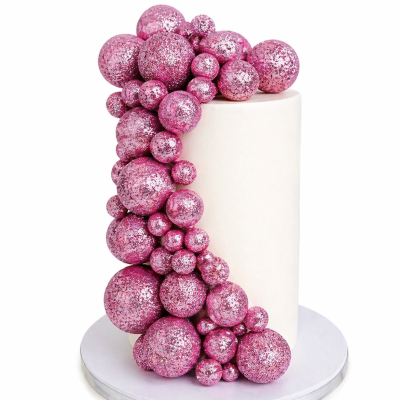 Bolo cilíndrico branco com decoração de bolas cor-de-rosa brilhosas.