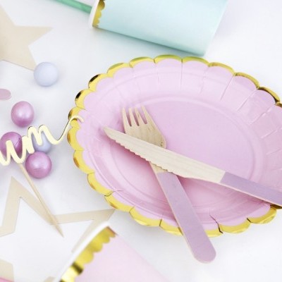 Prato rosa com borda dourada e talheres de madeira sobre mesa decorada para festa