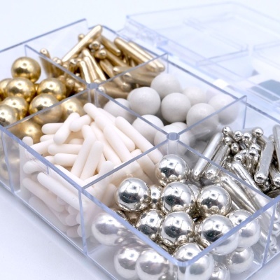 Caixa transparente com bolas e cilindros metálicos dourados, prateados e brancos organizados.