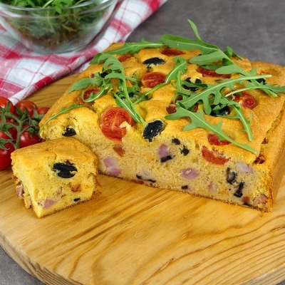 Bolo salgado quadrado com tomate cherry, azeitonas e rúcula num tabuleiro de madeira