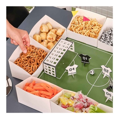 Caixas brancas com vários petiscos junto a jogo de futebol em miniatura