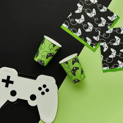 Copos, guardanapos e prato de papel com tema de videojogos, decorados com comandos e padrões em verde, preto e branco