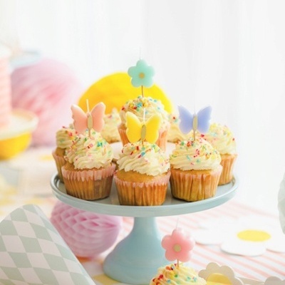 Cupcakes decorados com toppers de borboletas e flores sobre suporte azul claro em ambiente festivo