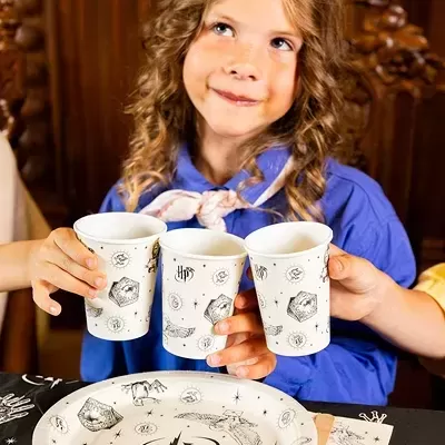 Criança segurando copos de papel com tema Harry Potter e prato correspondente sobre mesa