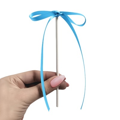 Palito branco com fita azul amarrada segurado por mão com unhas pintadas de rosa claro.