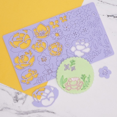 Placa stencil lilás com formas de flores e folhas sobre superfícies amarela e branca marmorizada, base circular verde decorada com flores.