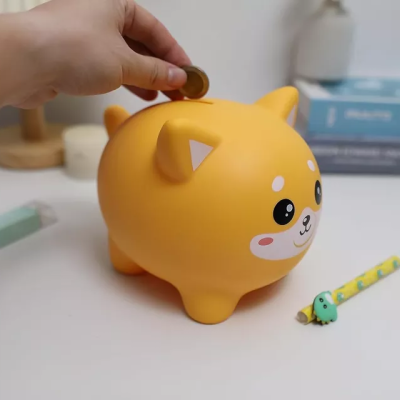 Mealheiro cão amarelo de plástico numa mesa branca com mão a colocar moeda