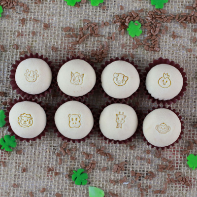 Mini bolos brancos com desenhos de animais em forminhas marrons sobre pano rústico com confetes