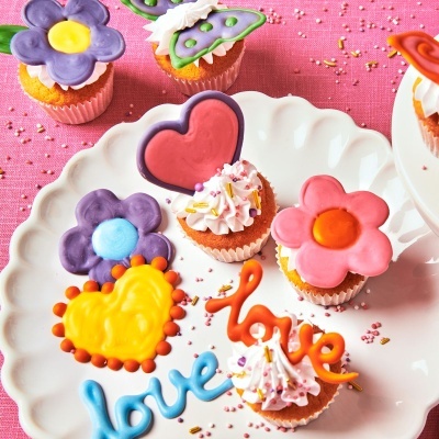 Mini bolos decorados com flores e corações coloridos em prato branco sobre fundo rosa