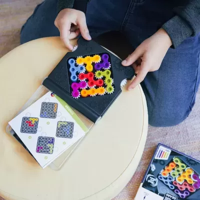 Jogo de peças coloridas de plástico em tabuleiro preto com cartas ilustrativas sobre almofada bege