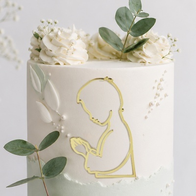 Bolo branco decorado com chantilly, folhas verdes e figura dourada de pessoa em oração
