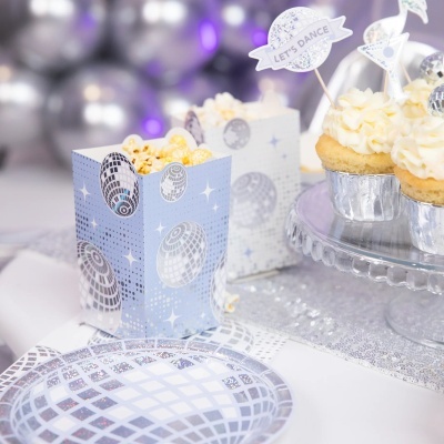 Caixas azuis decoradas com bolas de espelhos prateados, prato descartável e cupcakes decorados prateados com texto LETS DANCE