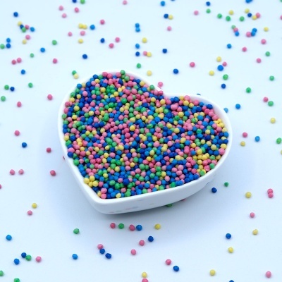 Tigela branca em forma de coração cheia de confeitos coloridos espalhados ao redor