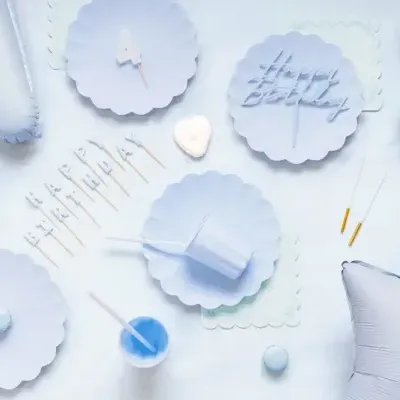 Artigos de festa azuis claros com pratos, copos, velas e balões