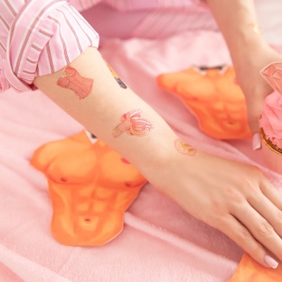 Tatuagens temporárias em braço com almofadas laranja ao fundo