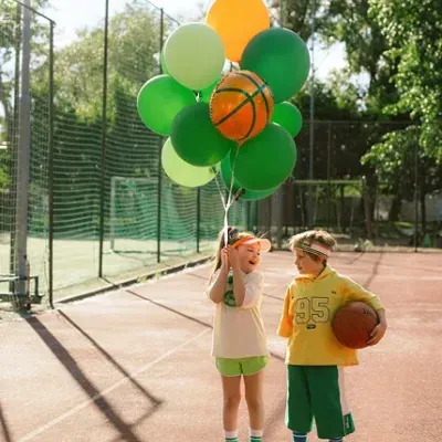 crianças em campo desportivo com balões verdes e amarelos e bola de basquetebol