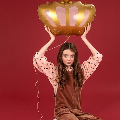 Menina jovem sentada a segurar balão dourado em forma de coroa com coração