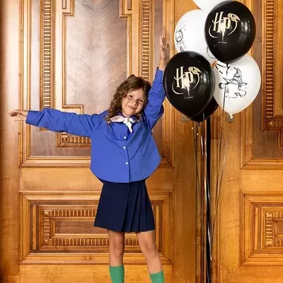Menina alegre ao lado de balões pretos e brancos com símbolos HP em ambiente com parede de madeira