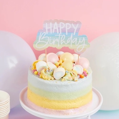 Bolo de aniversário colorido com marshmallows e topper 'HAPPY Birthday' em fundo com balões brancos