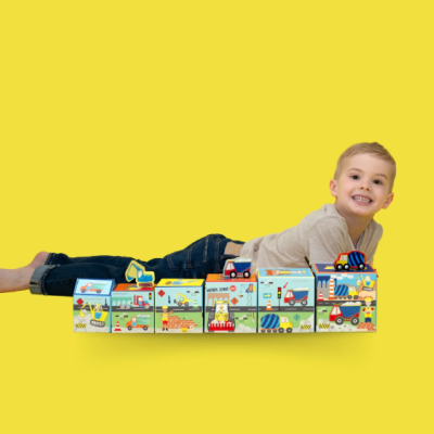 Criança a brincar com blocos coloridos de construção com imagens de veículos e sinais, sobre fundo amarelo