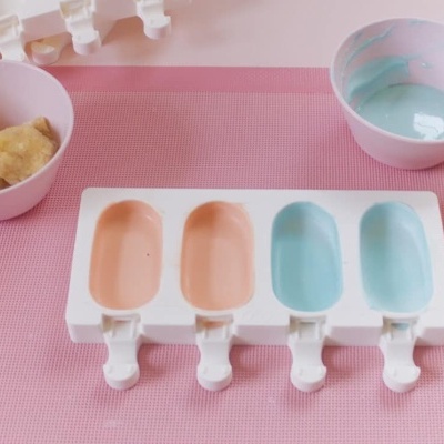 Forma de silicone para gelados com mistura colorida ao lado em tigelas cor de rosa