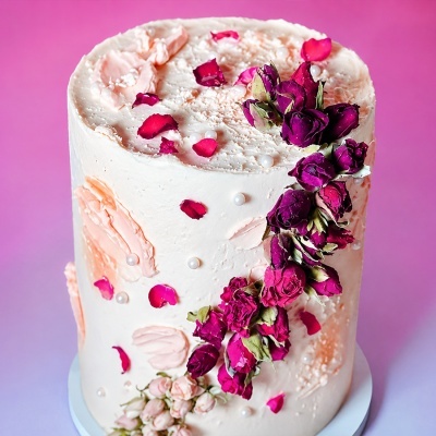 Bolo decorado com rosas secas e pérolas comestíveis sobre fundo rosa.