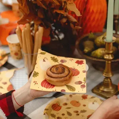 Rolo de canela em guardanapo e prato com padrão de outono, candeeiro, vela e decoração outonal