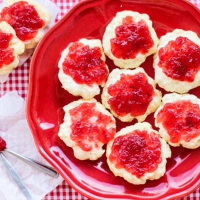 Biscoitos com compota de morango em prato vermelho sobre toalha xadrez