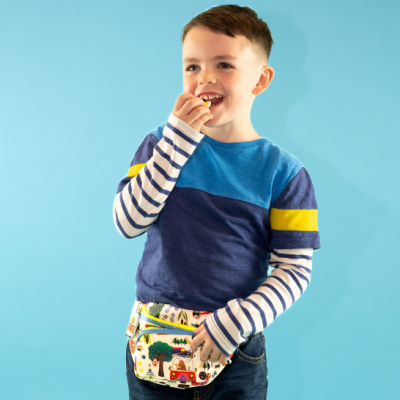 Criança com camisola azul e pochete estampada, a comer, com fundo azul