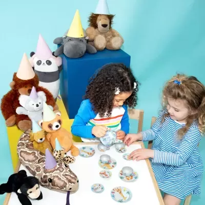 Peluches de animais com chapéus de festa e crianças a brincar de chá