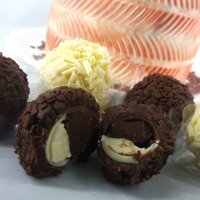 Trufas de chocolate preto e branco com recheio cremoso, sobre superfície branca com objeto decorativo laranja ao fundo