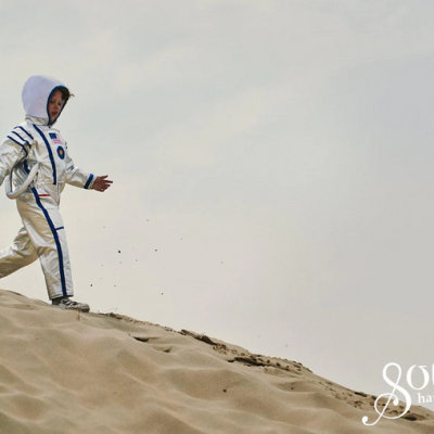 Criança com fato de astronauta a correr numa duna de areia