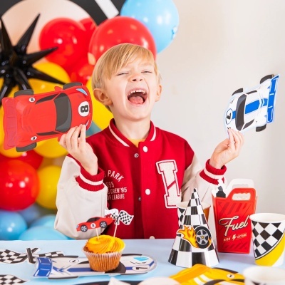 Criança feliz segurando balões em forma de carros numa festa com decoração de corrida e balões coloridos.