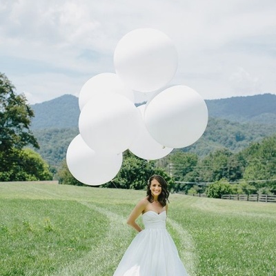 Mulher de vestido de noiva branco segurando balões brancos em campo verde