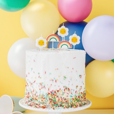 Bolo branco com granulados coloridos e velas decorativas, balões coloridos ao fundo