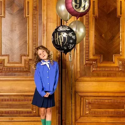 Menina com roupa azul e balões ao fundo com temas de Harry Potter
