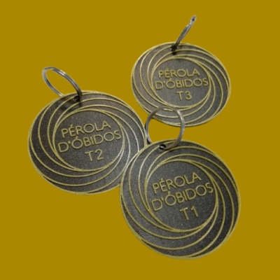 Três etiquetas redondas de metal com texto Pérola D'Óbidos e tamanhos T1, T2, T3 em fundo amarelo
