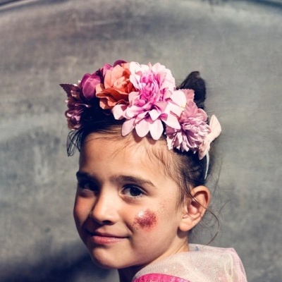 Menina com tiara de flores coloridas e capa rosa transparente