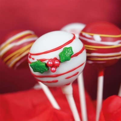 Três cake pops decorados com glacê branco e vermelho, uma com detalhes em verde e vermelho que parecem folhas e bagas.