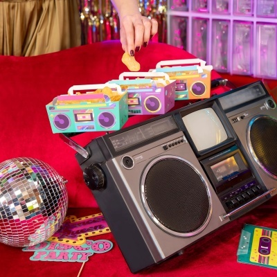 Caixas de papelão coloridas com batatas fritas em rádio boombox retro no sofá vermelho com bola de espelhos e decoração disco.