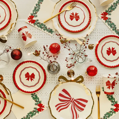 Conjunto de loiça decorada com temas natalícios, mostrando pratos, chávenas e talheres em tons de vermelho, branco e dourado numa mesa decorada.