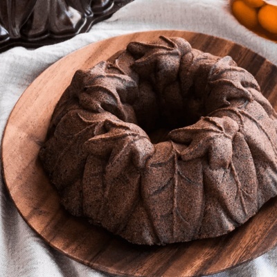 Bolo bundt castanho decorado em forma de folhas num prato de madeira sobre tecido claro