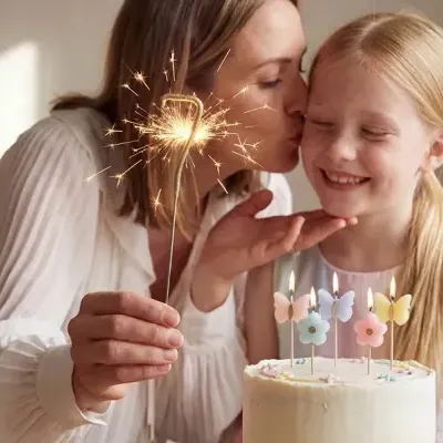 Mulher com vela de faísca e menina sorridente junto a bolo com velas decorativas
