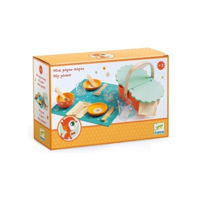 Jogo de piquenique infantil com cesta verde, pratos e talheres de madeira, copos transparentes e toalha azul com flores.