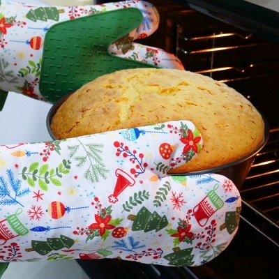 Luva de forno com padrão natalício segurando bolo amarelo num tabuleiro redondo preto