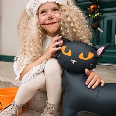 Criança vestida para Halloween com balão inflável de gato preto e acessórios laranja