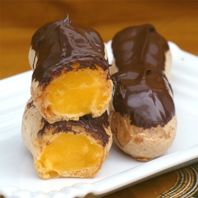 Dois éclairs com chocolate e recheio amarelo num prato branco